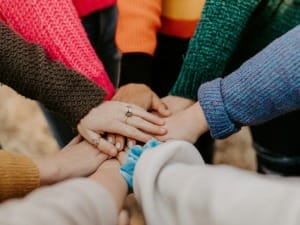 A picture of various people putting their hands in the middle of the group in a show of teamwork.
