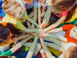 A picture of multiple children putting their hands in the middle with a System C logo.
